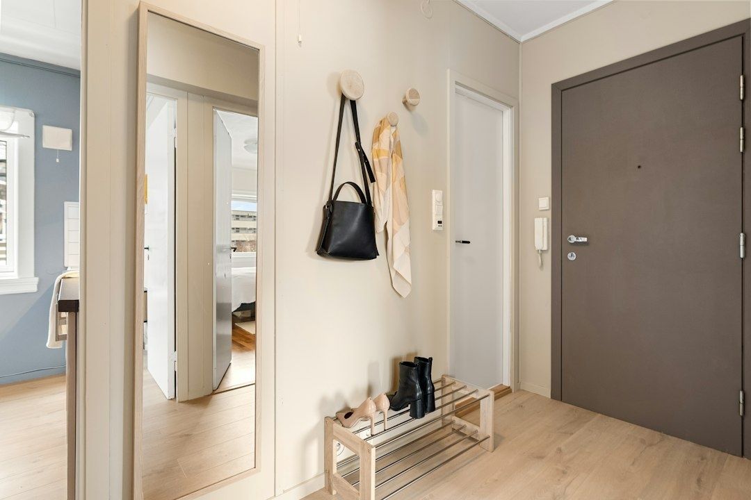 Ljus hall med stor spegel, krokar, skoförvaring och mörk entrédörr