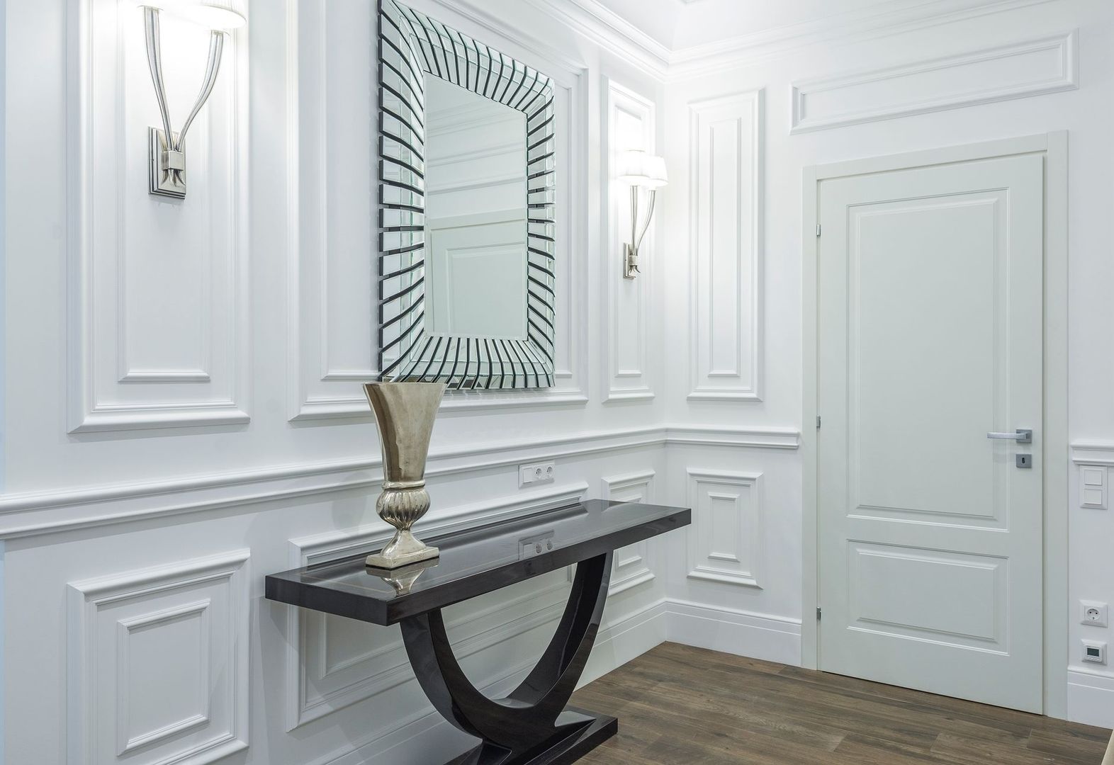 Elegant hall med smal konsol, spegel och vit dekorpanel